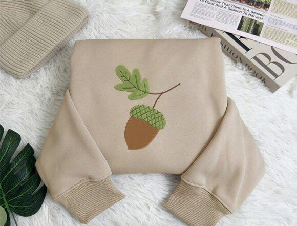 Beige sweatshirt with fall embroidery designs featuring an acorn and leaf motif