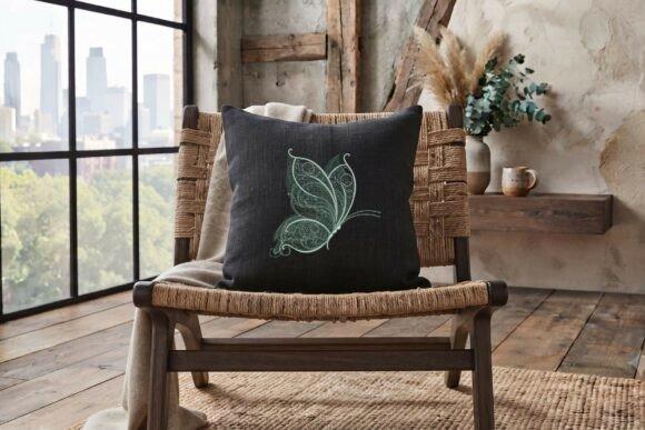 Black cushion with delicate butterfly embroidery design on a woven chair in a rustic room