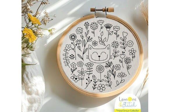 Hand embroidery designs featuring a whimsical cat face surrounded by wildflowers in a wooden hoop