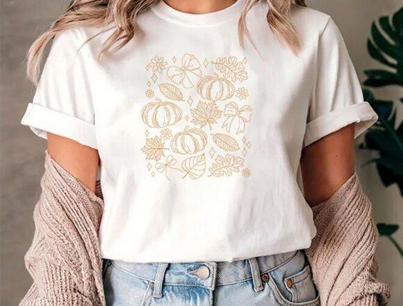 Fall embroidery designs featuring delicate pumpkin, leaf, and bow linework on a white t-shirt