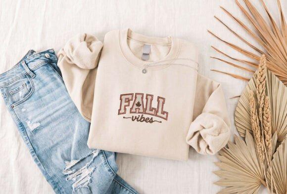 Beige sweatshirt with fall embroidery designs featuring bold FALL lettering and a maple leaf accent