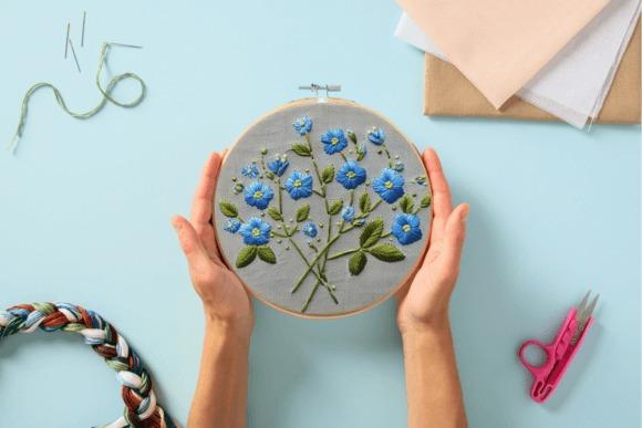 Hand embroidery designs featuring blue forget-me-not flowers stitched on fabric in a hoop