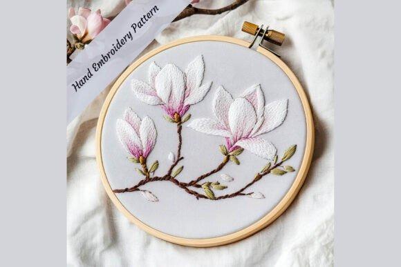 Hand embroidery designs showing a magnolia blossom branch with white and pink flowers in a wooden hoop