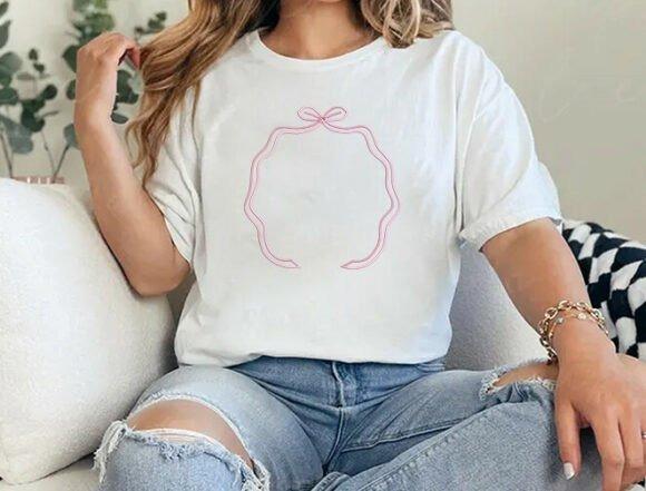 White t-shirt with a pink monogram embroidery design featuring a curved frame and a single top bow