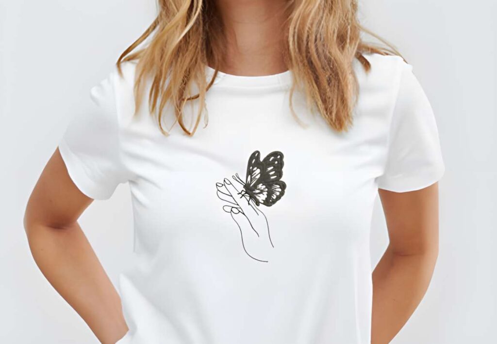 Black butterfly embroidery design on white t-shirt held by hand outline — machine embroidery designs for various styles