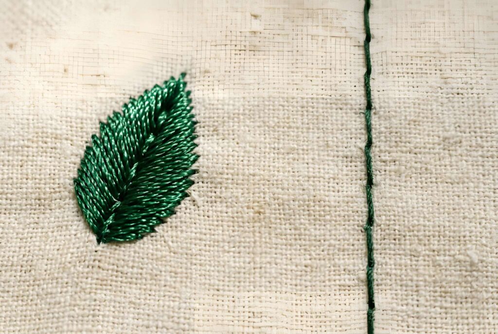 Green machine embroidery thread stitched leaf with sheen next to matte sewing thread on beige fabric