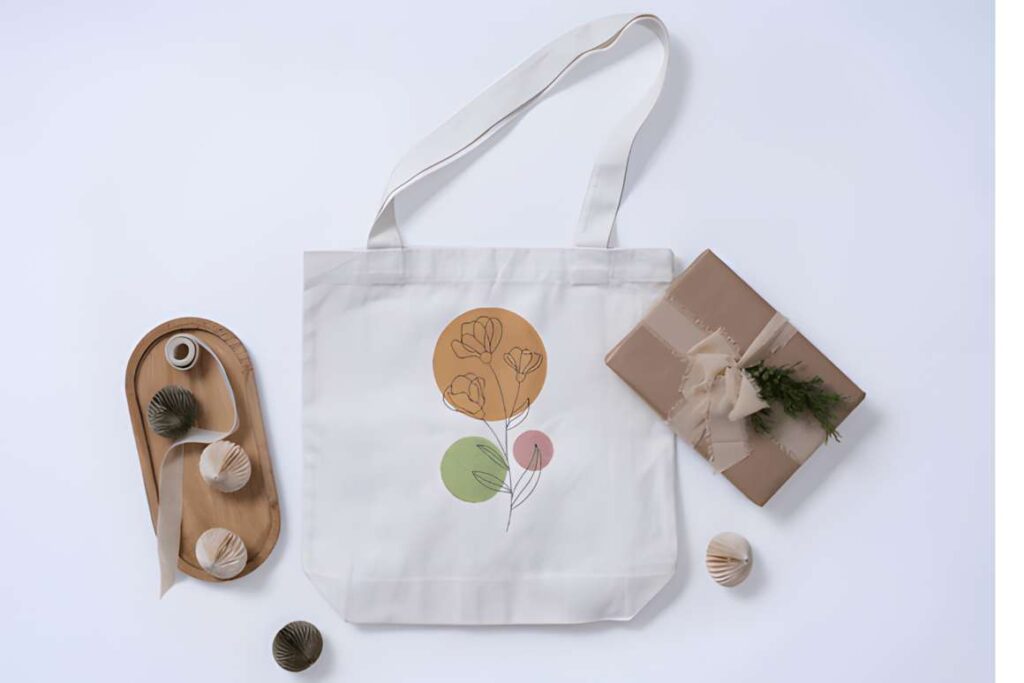 White tote bag with floral and leaf machine embroidery designs for various styles, surrounded by decorative items