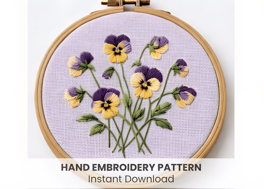 Hand embroidery patterns of pansy flowers in purple and yellow stitched on fabric in an embroidery hoop